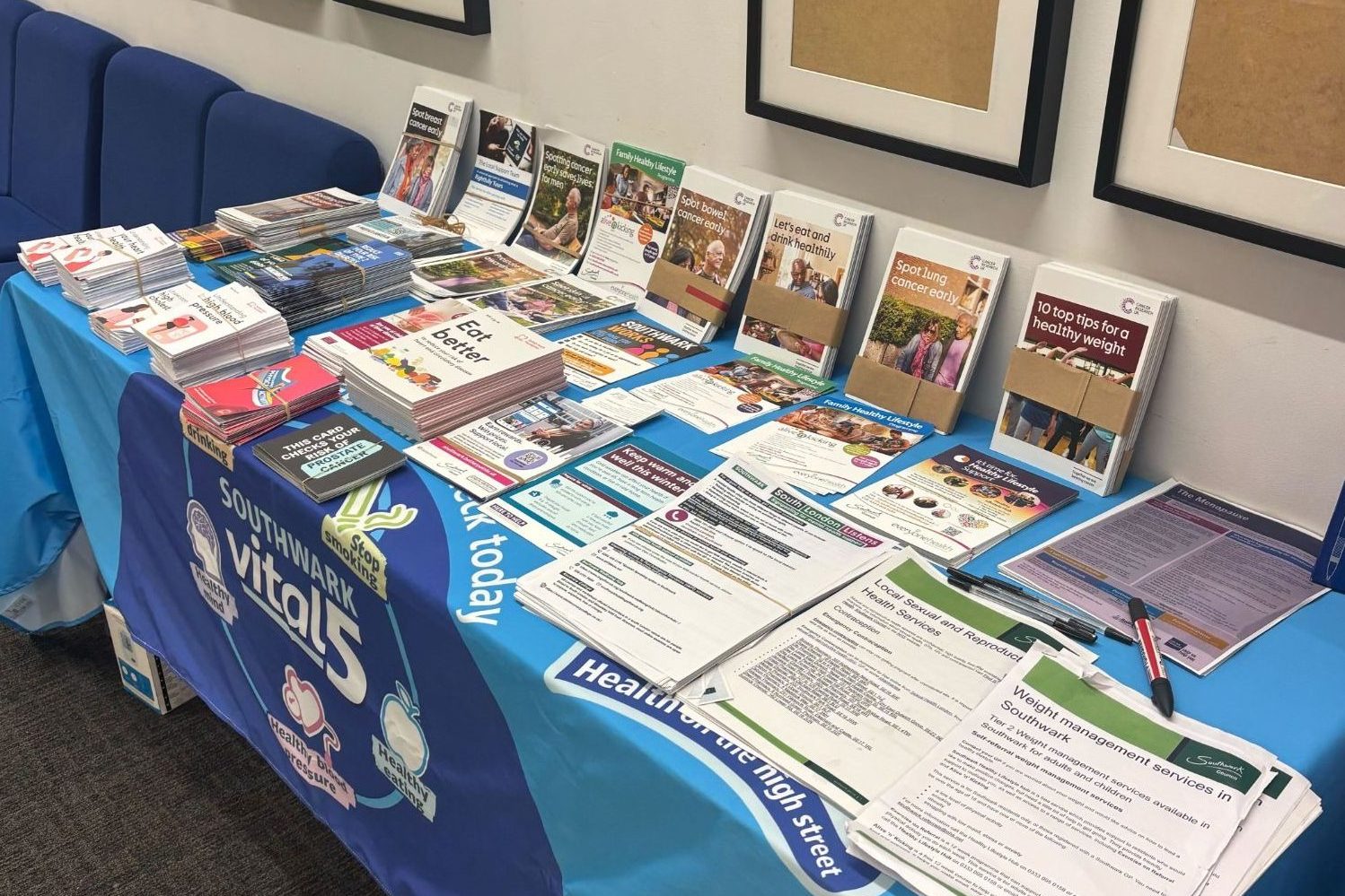A table covered with a blue cloth displaying various pamphlets, brochures, and informational sheets related to health services.