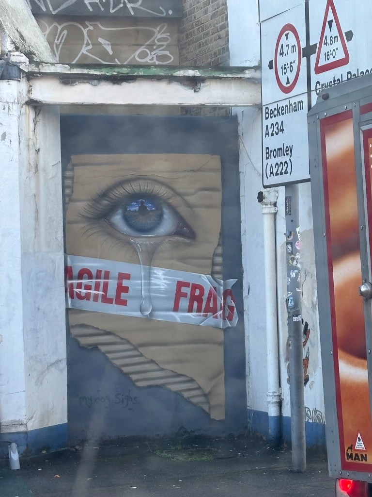 A mural depicting a close-up of an eye with a tear, surrounded by a torn paper effect. A piece of tape marked 'FRAGILE' crosses over the image.