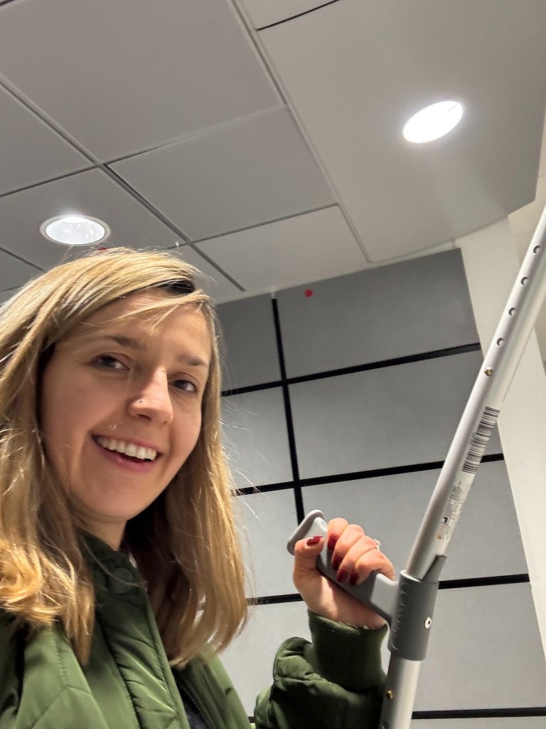 A woman smiling while holding a gray crutch 